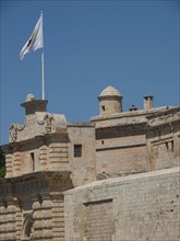 Imposing stone walls of a historic fortress with a view of wide towers and a waving flag under a