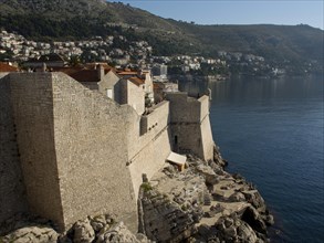 Massive walls of a historic coastal fortress with a view of the sea and surrounding buildings, the