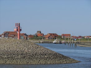 A harbour with red houses and boats moored on the shore, with a clear blue sky, Baltrum Germany