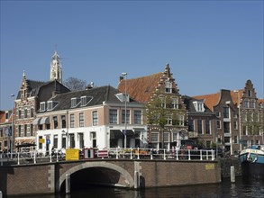 Historic buildings along a river with bridge and boats under a blue sky, Haarlem, Netherlands