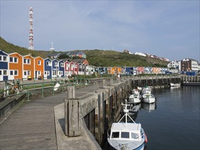 Harbour with colourful houses and fishing boats on a wooden pier in a hilly landscape under a blue