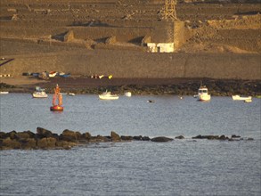 Boats and buoys on the sea in front of a rocky coastline at sunset, Lanzarote with a hisotric