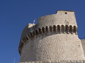 Massive stone fortress with flag against a blue sky, the old town of Dubrovnik with historic