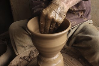 Hands molding clay on a pottery wheel, creating a vase, showcasing the art of crafting pottery