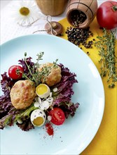 A blue plate with a salad topped with meatballs, quail eggs, tomatoes, and herbs arranged