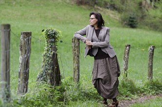 Elegant Business Woman Standing on a Forest Path and Leaning on a Fence in the Nature in