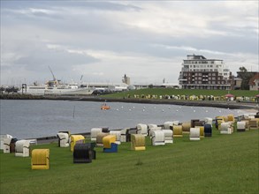 Beach chairs in a meadow near a town with a view of the harbour, ships and cloudy sky, Cuxhaven,