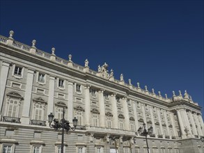Wide frontal view of a classical baroque building with numerous windows and sculptures under a blue