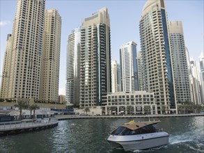 A boat sails on a river past a row of modern high-rise buildings and skyscrapers, dubai, arab