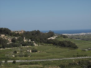 Vast green landscape with hills, trees and a city on the horizon under a clear sky, the town of