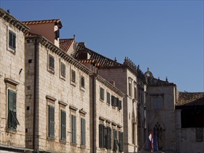 Street view of historic buildings with stone facades and shutters under a blue sky, the old town of