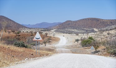 Road with road sign Attention river crossing, gravel track leads through barren dry landscape with
