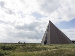 Modern pyramid-shaped building in a meadow under a partly cloudy sky, Spiekeroog, Germany, Europe