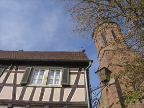 Traditional tower and half-timbered house surrounded by trees under a blue sky, historic