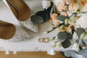 Silver shoes and wedding rings on a white table next to a bouquet of flowers