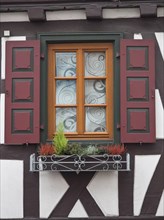Close-up of a window with red shutters and decorative flower box of a half-timbered house, kandel,
