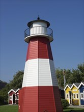A lighthouse with red and white stripes next to colourful little houses on a sunny day, Heligoland,