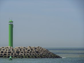 A single green lighthouse next to concrete breakwaters with calm sea in the background, lighthouses