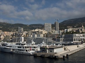 Sea harbour with yachts and modern buildings in the background surrounded by mountains and slightly