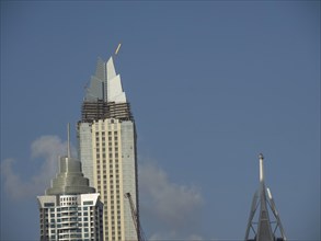 Partially completed modern building with crane in front of blue sky, dubai, arab emirates