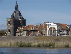Historic tower and building with red tiled roofs on a riverbank under a blue sky, Enkhuizen,