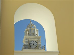 The clock of a church tower seen through a yellow arch, contrasted against the blue sky in
