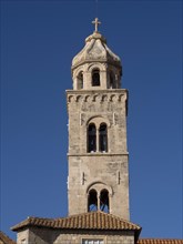High stone church tower with a cross at the top, in front of a bright blue sky, the old town of