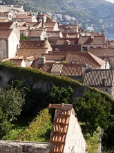 Historic city view with red tiled roofs and green vegetation, embedded in a mountainous landscape,