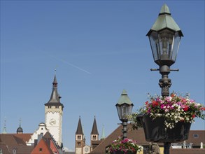 Flower decorated lamps in front of a blue sky with church towers and historical buildings in the
