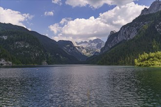 Large, calm lake surrounded by forested mountains and a cloudy sky, turquoise green mountain lake