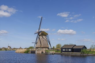 Rural scene with an old windmill on a lake and a small blue house under a clear sky, windmills of