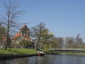 Landscape with a riverside church, a picturesque bridge and a boat on the water, Haarlem,