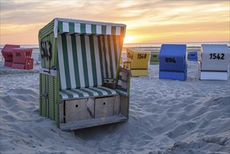 A green beach chair in a sand pit, surrounded by colourful beach chairs, at sunset, summer evening