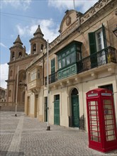 Historic street with a church in the background, ornate facades and a red British telephone box,