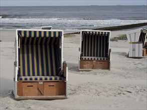 Three beach chairs with striped awnings stand on the beach in front of the sea under a slightly