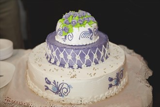 Elegant two-tier cake adorned with purple roses and intricate lace-like icing decorations
