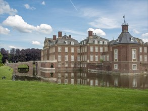 Historic castle with moat and reflection in the water, surrounded by lawn and blue sky with clouds,