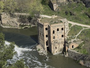 An old, half-ruined building or ruin by a river with a small waterfall, embedded in nature, toledo,