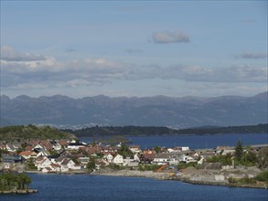 City along a fjord, surrounded by mountains and clouds, with clear blue sky, houses on small island