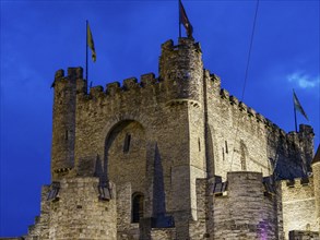 Illuminated historic castle with flags against dramatic night sky, blue hour in a medieval town