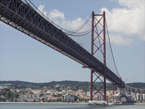 Red steel bridge overlooks a coastal city with blue sky and clouds, Lisbon, Portugal, Europe