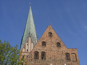 Church tower and gable of a brick gothic church with trees and blue sky in the background, red