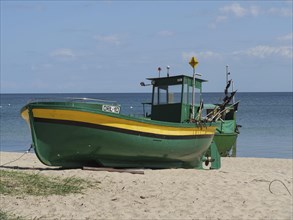 Two green and yellow fishing boats standing near the sea on a sandy beach, green and yellow fishing