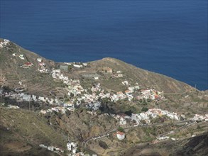 Panorama of a coastal village with houses on rolling hills and the ocean in the background, the