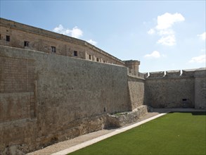 Massive stone walls of a fortress with a visible courtyard on a sunny day, the town of mdina on the