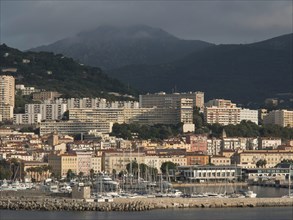 Coastal town with harbour in front of a mountain backdrop under a cloudy sky, Corsica, ajaccio,