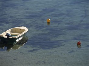 A small boat floats on clear water surrounded by buoys that are reflected in the water, the old