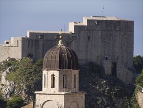 View of a fortress and a church with a dome on a rocky, green hill, the old town of Dubrovnik with
