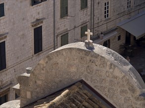 Close-up of a stone roof with a cross and old buildings in the background, the old town of