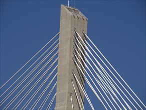 Modern cable-stayed bridge with a high concrete tower and numerous steel cables under a clear sky,